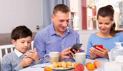 Fototapeta na wymiar Parents and teen son using phones at kitchen. High quality photo