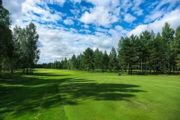 Fototapeta premium Golf course, landscape, green grass on the background of the forest and a bright sky with clouds. High quality photo