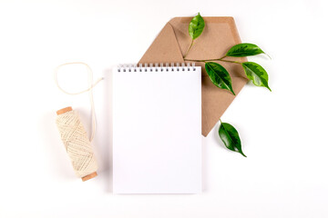 Notebook, recycled paper envelope and spool of plain coarse thread lie on white surface with sprig of green plant. Ecology concept, recyclable, no waste, office, business. Selective focus. Copy space.