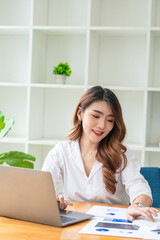 Young asian business woman working on computer laptop in office room with paperwork document on desk