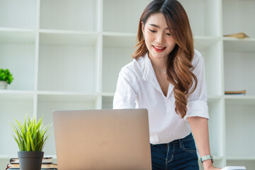 Young asian business woman working on computer laptop in office room with paperwork document on desk