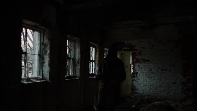 silhouette of a man in a dark cloak walking through an abandoned building with an ax. The concept for the autumn holiday halluin.