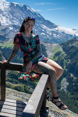 Naklejka premium View of a brunette young woman on the Mouunt Fremont Fire Lookout in Mount Rainier National Park. The peak of the mountain is covered in snow and below is fields of green grass.