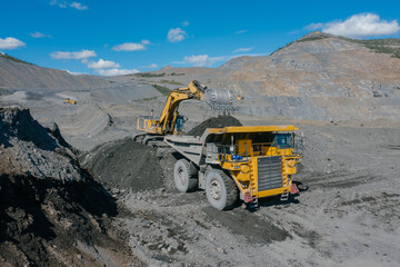 An excavator loads ore into a dump truck. The action takes place in an open pit.
