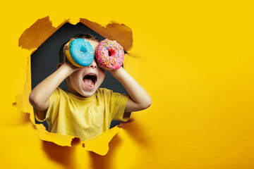 Happy cute boy is having fun played with donuts on Yellow background wall. Bright photo of a boy....