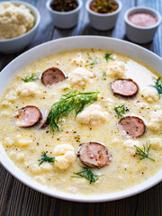 Cauliflower soup with sausages on wooden table
