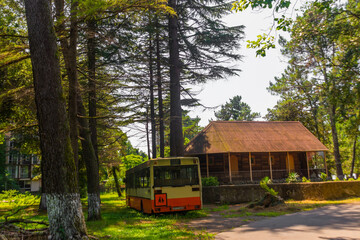 Obraz premium KOBULETI, GEORGIA: A wooden Orthodox church and an old German bus in a shady park.