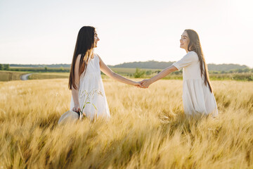 Portrait of two sisters in white dresses with long hair in a field