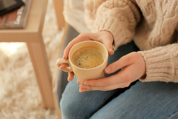 Young woman with cup of coffee at home, closeup