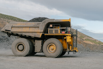 Obraz premium A dump truck loaded with ore drives through an open pit.