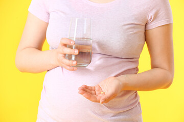 Young pregnant woman with pills and glass of water on color background