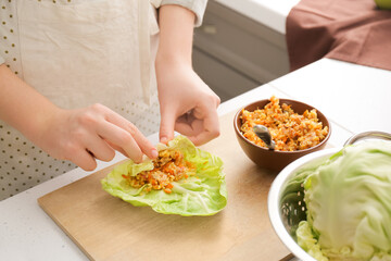 Woman preparing tasty stuffed cabbage roll on table in kitchen, closeup