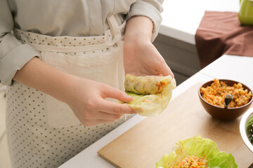 Woman preparing tasty stuffed cabbage roll on table in kitchen, closeup
