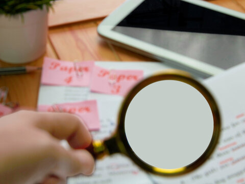 blurred paperwork on wooden table and blurred hand holding magifier