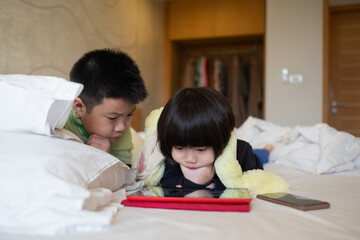 two chinese children addicted tablet, asian child watching telephone together on their bed, kid using smartphone
