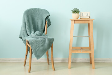 Knitted plaid on chair and table with calendar near color wall
