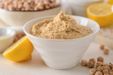 Bowl with tasty hummus on light wooden background, closeup