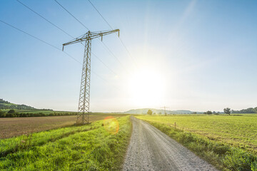 Power line in rural landscape with scenic sun rays and lens flare symbolising green, renewable energy