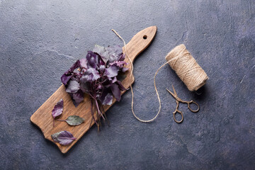 Wooden board with fresh basil, rope and scissors on dark background