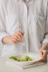 Woman eating tasty pesto pasta at table, closeup