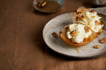 Horizontal side view of tasty vegetarian dessert. Sweet baked pears with ice cream and walnuts. Honey on ceramic plate on wooden background. Served delicious breakfast, copy space