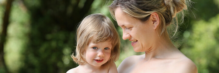Happy little smiling child in the arms of the mother on a natural background