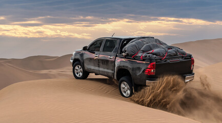 a black pickup truck is going up from a sand dune and splashing sands on air and around in dasht e...