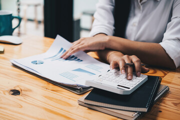 Close up asian female accountant or banker making calculations with calculator. Savings, finances and economy concept through a laptop