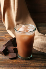 Glass of tasty chocolate milk on wooden background