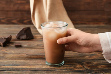 Woman with glass of tasty chocolate milk on wooden background