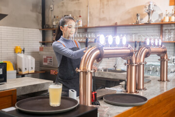 Portrait of Asian bartender girl hand at beer tap pouring , waitress or staff serve and craft, draught beer in glass serving in a restaurant or pub beer