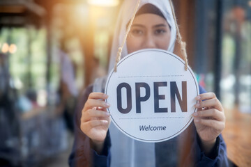 Muslim woman owner shop holding open sign in front of door café and shop, new normal and start...