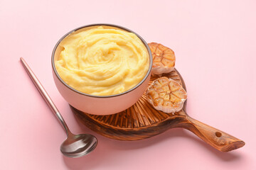 Bowl of tasty mashed potatoes with garlic on color background