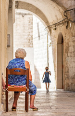Grandmother waiting for her granddaughter on the doorstep in the narrow streets of Bari old town,...