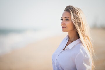 A tanned girl in a blue swimsuit and a light shirt enjoys the summer at the seaside