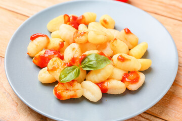 Delicious gnocchi with tomato sauce in plate on wooden table