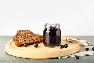 Jar with delicious black currant jam and bread on color wooden table