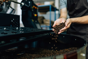 High angle view of the master enjoying burned beans aroma while holding them in hands. He standing near industrial technical equipment. Factory concept