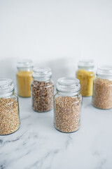 clear pantry jars with different types of grains in them including quinoa rice buckwheat couscous and barley, simple ingredients concept