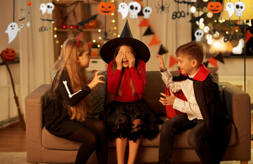 halloween, holiday and childhood concept - smiling boy and girls in costumes playing and scaring...