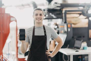 Professional master barista holding phone screen near roasting coffee beans in the best machine