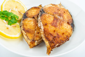 Pan-fried mackerel pieces on a plate on white background