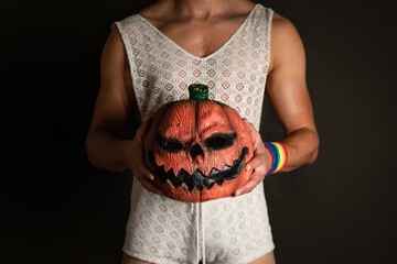 man disguised as woman, with pumpkin mask in hand of halloween, and wristband with lgbt colors, in...