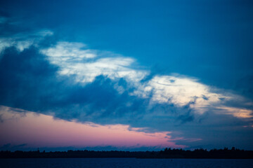 Evening river landscape. Calm water and dramatic sky with clouds. Trees grow on the nearest shore. There is a copy space