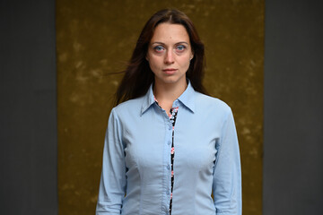 Photo of a serious brunette woman in a blue shirt on a dark golden background looking directly at the camera - 454277834