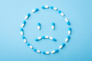 Sad face made of pills on blue background. Concept of ill person, disease, treatment, capsules and medication