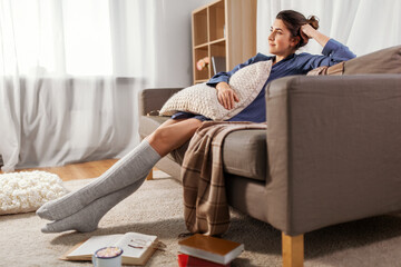 people and leisure concept - young woman with pillow and books on floor resting on sofa at home