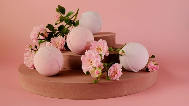 Bath bombs with rose extract.Flower Bath Bombs.Organic vegan eco cosmetics.Pink bath bombs and pink rose flowers on burgundy pedestal on a light pink background. Organic natural cosmetics with rose ex