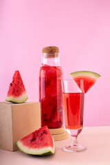Watermelon drink in a glass with fruit decor and a bottle with berry slices on pink background. Fresh red lemonade to drink during hot day. Cooling beverage. Vertical.