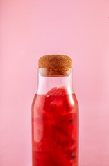 Femail hands holding glass bottle with watermelon drink on pink background. Stylish vertical concept with red juice. Fresh cooling beverage with piece of fruits.